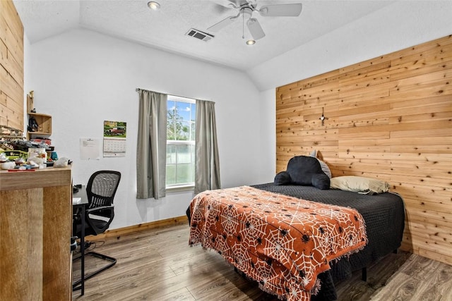 bedroom featuring lofted ceiling, hardwood / wood-style floors, wooden walls, and a textured ceiling