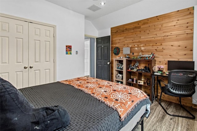 bedroom with hardwood / wood-style floors, wooden walls, vaulted ceiling, and a closet