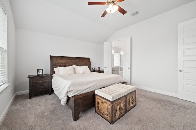 bedroom with ceiling fan, light colored carpet, vaulted ceiling, and ensuite bath