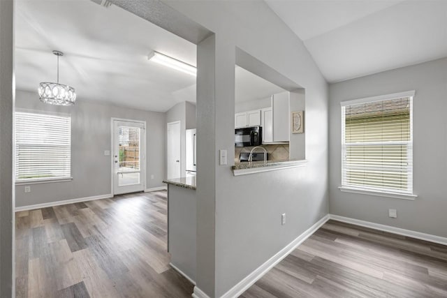 kitchen featuring lofted ceiling, white cabinetry, backsplash, light stone countertops, and decorative light fixtures