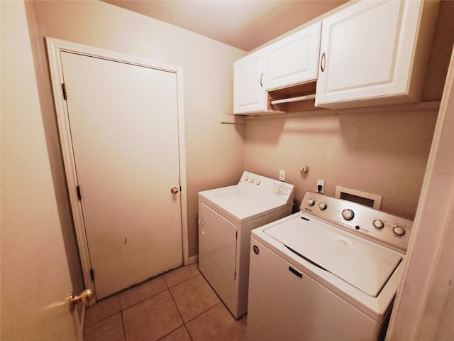 clothes washing area featuring washer and dryer, light tile patterned floors, and cabinets