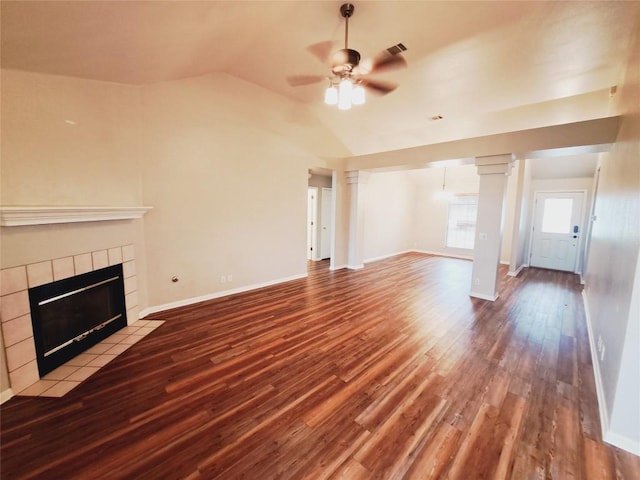 unfurnished living room with a tiled fireplace, lofted ceiling, hardwood / wood-style floors, and decorative columns