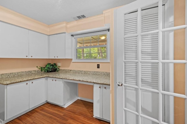 kitchen with wood-type flooring, light stone countertops, built in desk, and white cabinets