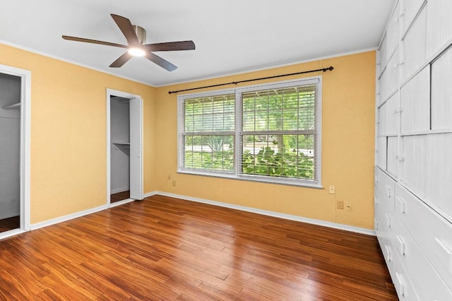 unfurnished bedroom with hardwood / wood-style flooring, ceiling fan, multiple closets, and crown molding