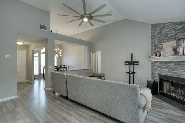 living room with light hardwood / wood-style floors, high vaulted ceiling, ceiling fan, and a stone fireplace