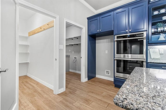 kitchen featuring crown molding, blue cabinetry, double oven, light stone countertops, and light wood-type flooring