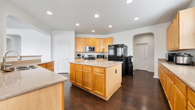 kitchen with dark wood-type flooring, sink, light stone counters, a kitchen island, and stainless steel appliances