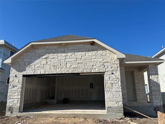 view of front of property with stone siding, roof with shingles, and an attached garage