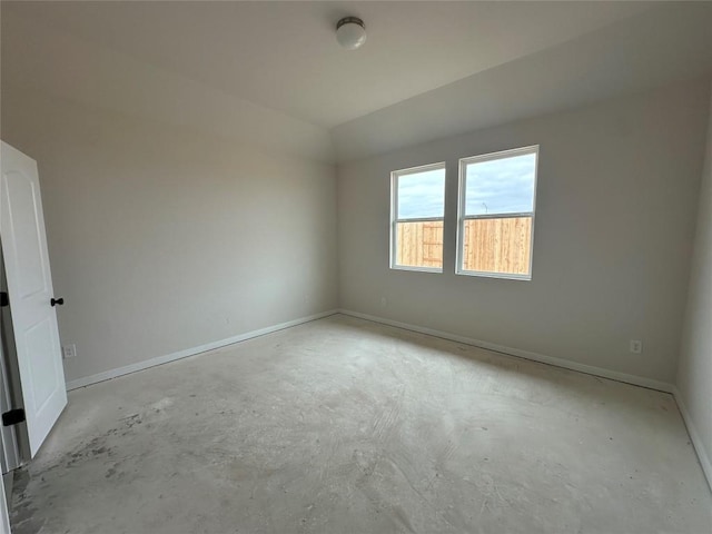 spare room with lofted ceiling, concrete floors, and baseboards