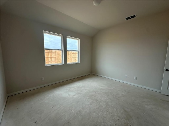 empty room featuring concrete flooring, visible vents, vaulted ceiling, and baseboards