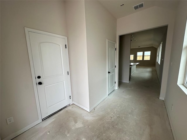 hall with vaulted ceiling, baseboards, visible vents, and unfinished concrete floors