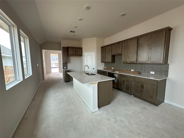 kitchen with a kitchen island with sink, a sink, baseboards, decorative backsplash, and unfinished concrete flooring