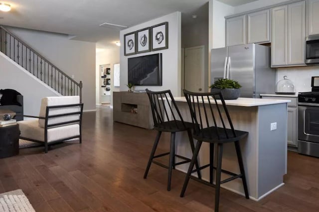 kitchen with gray cabinets, appliances with stainless steel finishes, a center island, a kitchen bar, and dark hardwood / wood-style flooring