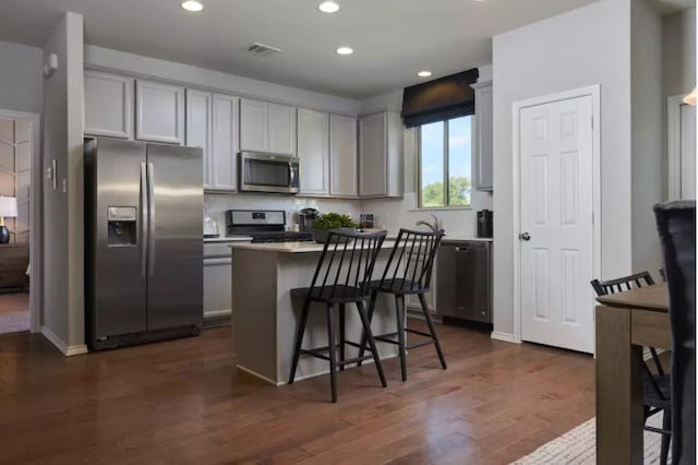 kitchen featuring a breakfast bar area, gray cabinets, appliances with stainless steel finishes, dark hardwood / wood-style floors, and a center island