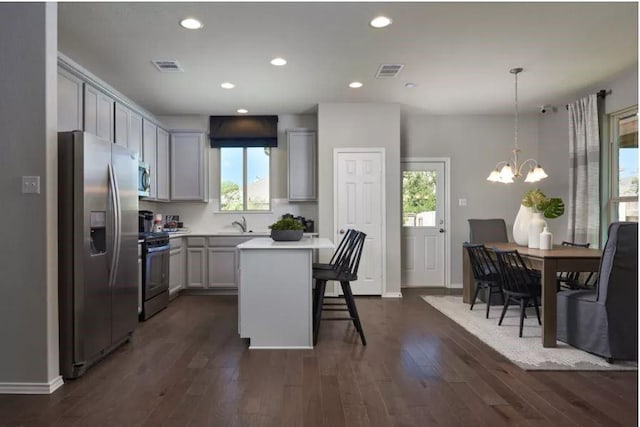 kitchen with dark wood-type flooring, gray cabinets, hanging light fixtures, stainless steel appliances, and a kitchen island