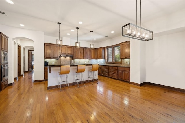 kitchen featuring tasteful backsplash, hanging light fixtures, light hardwood / wood-style flooring, and a center island