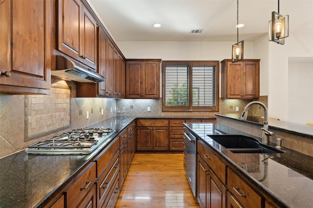 kitchen with sink, hanging light fixtures, light wood-type flooring, appliances with stainless steel finishes, and dark stone counters