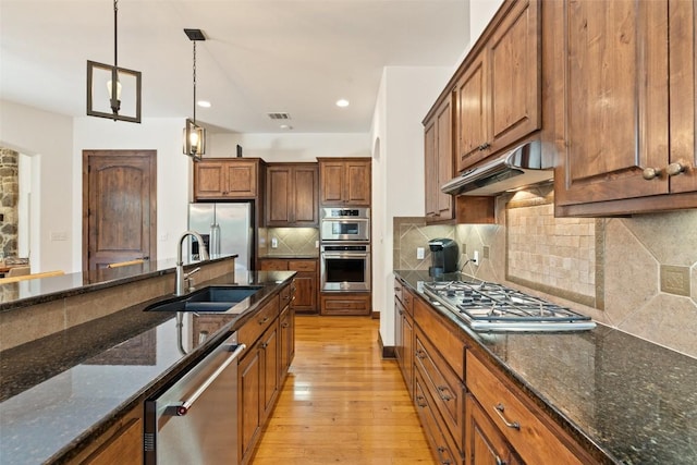 kitchen with hanging light fixtures, appliances with stainless steel finishes, sink, and dark stone countertops