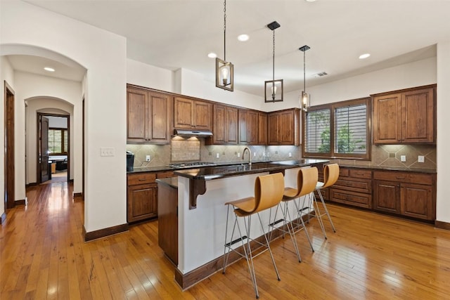 kitchen featuring a kitchen bar, hanging light fixtures, a kitchen island with sink, light hardwood / wood-style floors, and decorative backsplash