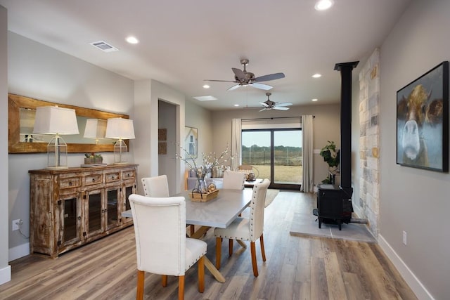 dining room with ceiling fan, a wood stove, and light wood-type flooring