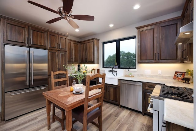 kitchen with appliances with stainless steel finishes, ventilation hood, sink, dark brown cabinets, and light hardwood / wood-style flooring