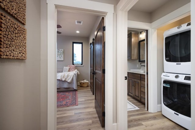 washroom with sink, a barn door, stacked washing maching and dryer, and light hardwood / wood-style flooring