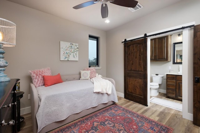 bedroom featuring ceiling fan, a barn door, connected bathroom, and light wood-type flooring