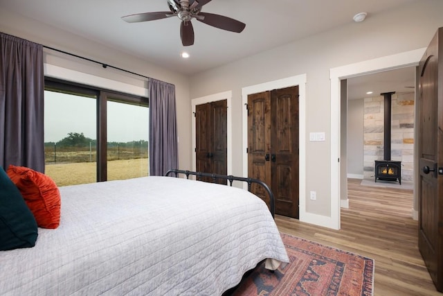 bedroom featuring a wood stove, two closets, ceiling fan, access to exterior, and light hardwood / wood-style floors