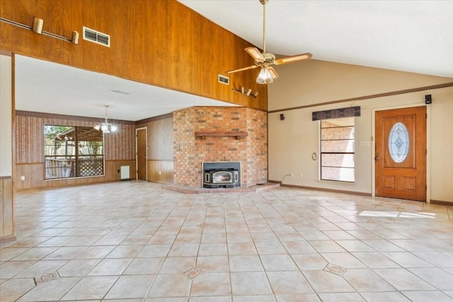 unfurnished living room featuring ceiling fan with notable chandelier, high vaulted ceiling, wood walls, a wood stove, and light tile patterned floors