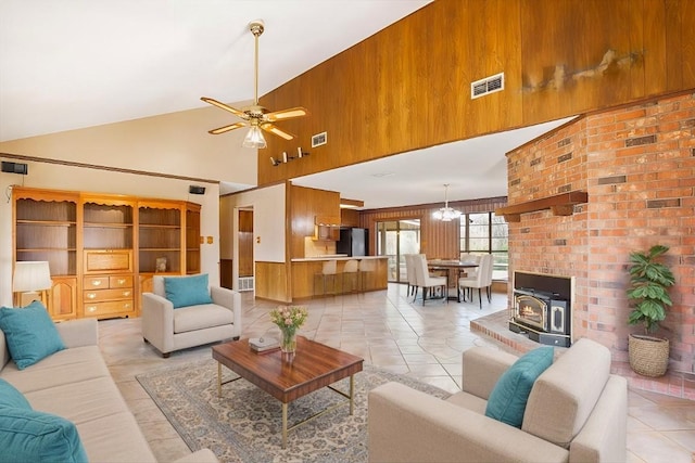 tiled living room featuring ceiling fan with notable chandelier, high vaulted ceiling, and wood walls