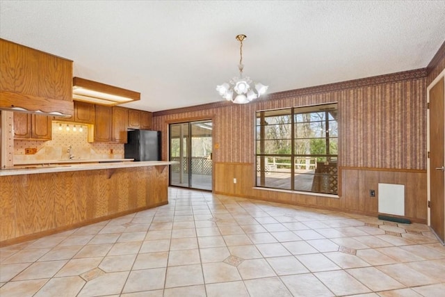 kitchen with pendant lighting, light tile patterned floors, a notable chandelier, black fridge, and kitchen peninsula