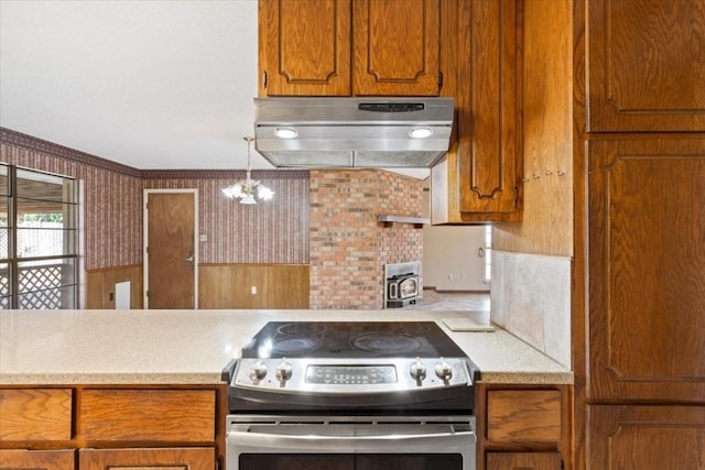 kitchen featuring stainless steel range with electric stovetop, hanging light fixtures, ventilation hood, and a wood stove