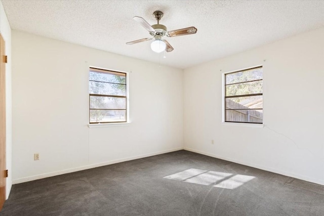 empty room with dark colored carpet, a wealth of natural light, ceiling fan, and a textured ceiling