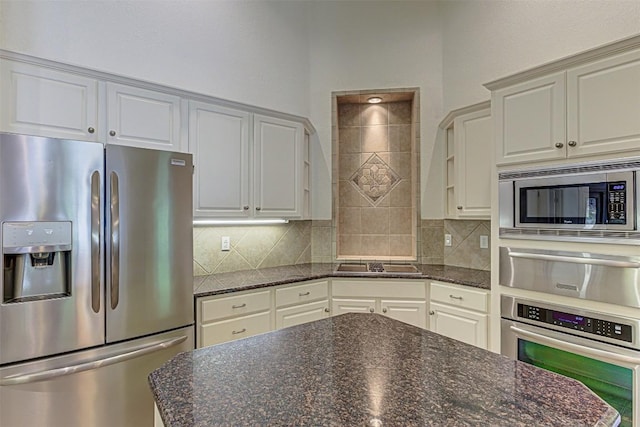 kitchen featuring tasteful backsplash, white cabinetry, stainless steel appliances, and dark stone countertops