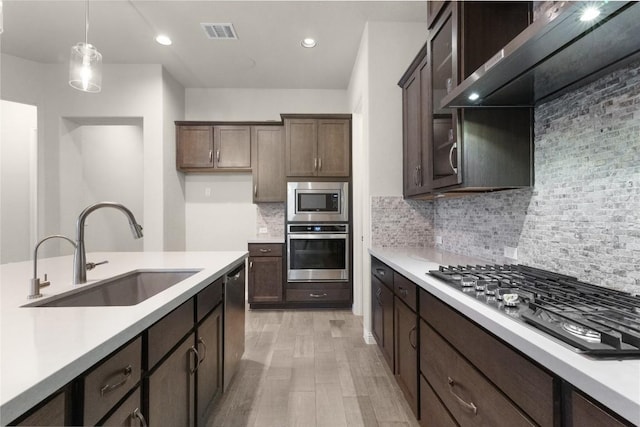 kitchen with dark brown cabinets, stainless steel appliances, sink, and hanging light fixtures