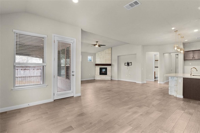 unfurnished living room with lofted ceiling, sink, ceiling fan, a fireplace, and light hardwood / wood-style floors