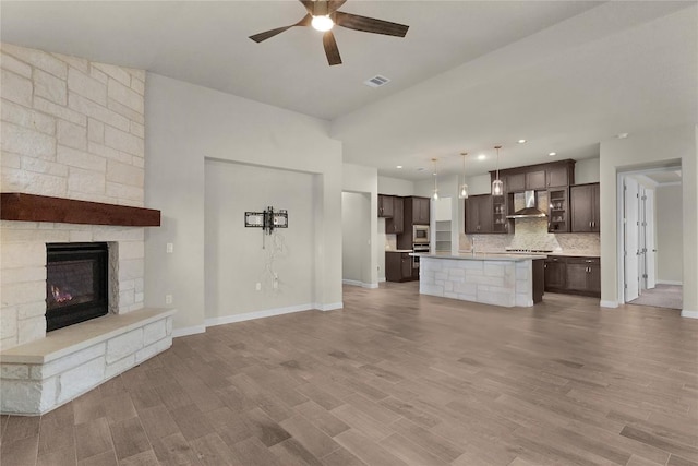 kitchen with dark brown cabinetry, decorative light fixtures, an island with sink, and wall chimney exhaust hood