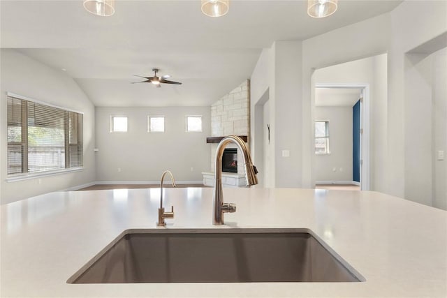 kitchen featuring ceiling fan, lofted ceiling, a stone fireplace, and sink