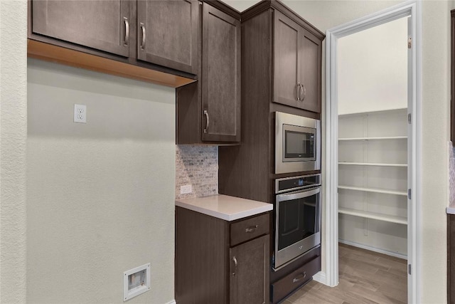 kitchen featuring dark brown cabinetry, stainless steel appliances, light hardwood / wood-style flooring, and backsplash