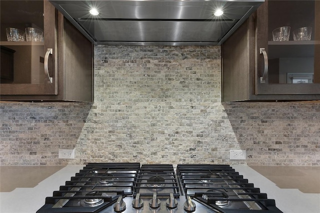 room details with gas stovetop, wall chimney range hood, dark brown cabinets, and tasteful backsplash