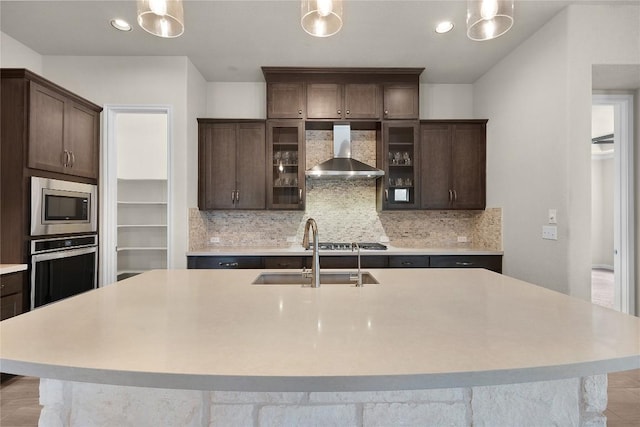 kitchen with pendant lighting, wall chimney range hood, sink, and appliances with stainless steel finishes