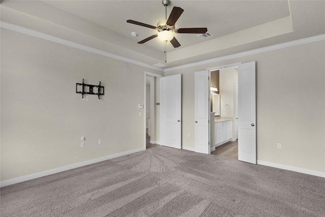 unfurnished bedroom featuring crown molding, light carpet, ensuite bathroom, and a tray ceiling