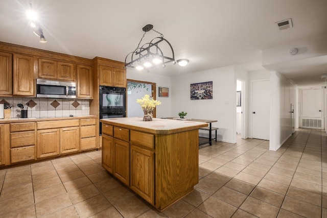 1000 Ledbetter St, Round Rock, TX 78681 - kitchen with stainless steel microwave, light tile patterned flooring, backsplash, a kitchen island, and decorative light fixtures
