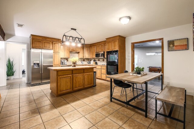 1000 Ledbetter St, Round Rock, TX 78681 - kitchen featuring appliances with stainless steel finishes, light countertops, light tile patterned floors, a center island, and tasteful backsplash