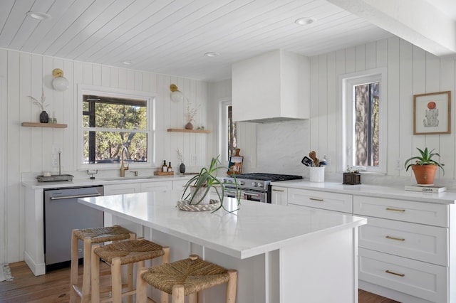 kitchen with a breakfast bar, sink, a center island, stainless steel appliances, and wall chimney exhaust hood