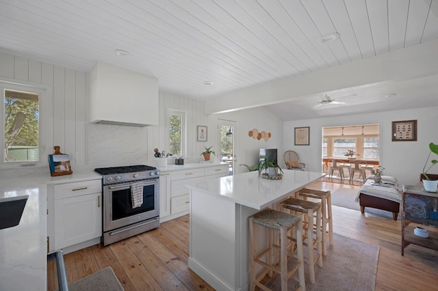 kitchen with white cabinetry, wall chimney range hood, light hardwood / wood-style floors, and stainless steel range with gas stovetop