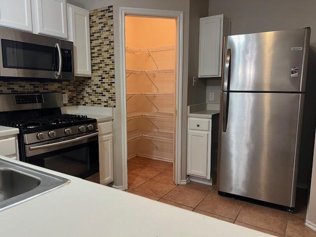 kitchen featuring tasteful backsplash, white cabinetry, appliances with stainless steel finishes, and light tile patterned flooring