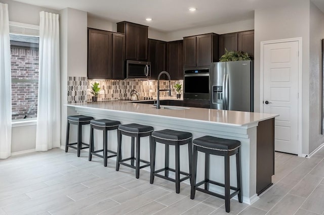 kitchen with a breakfast bar area, dark brown cabinets, stainless steel appliances, tasteful backsplash, and kitchen peninsula