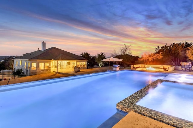 pool at dusk with an in ground hot tub, pool water feature, an outdoor fire pit, and a patio area