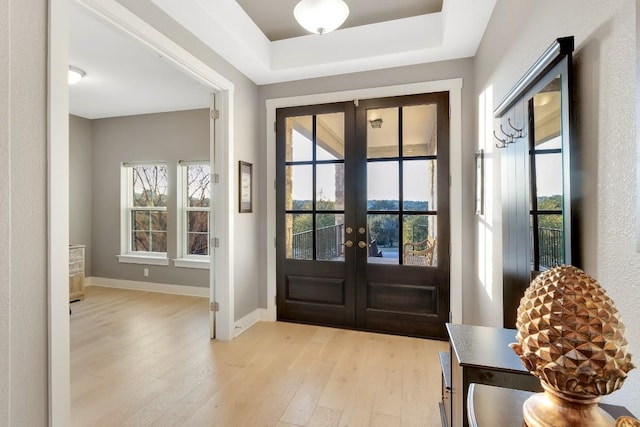 entryway featuring light hardwood / wood-style flooring, french doors, and a raised ceiling